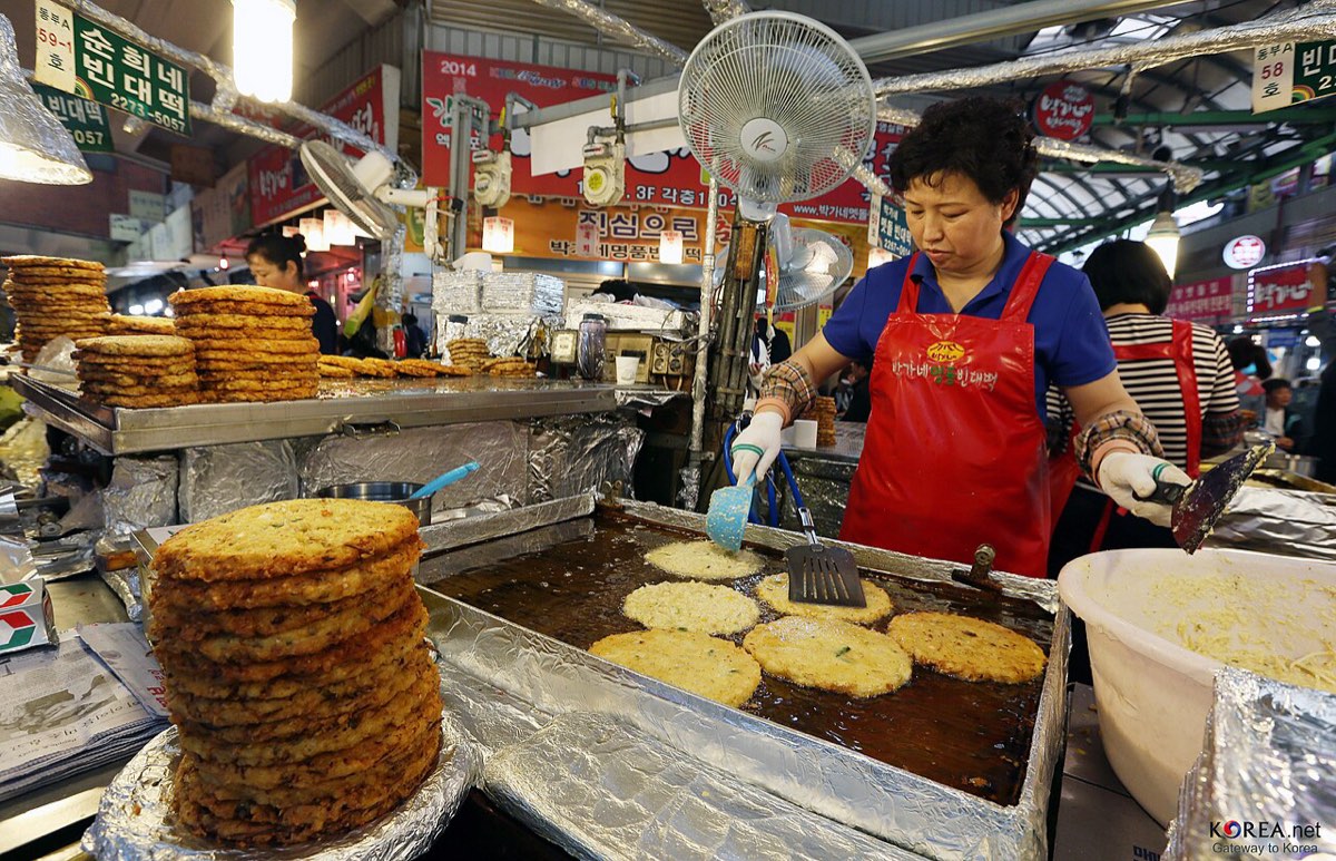 Stacks of freshly fried bindaetteok, thick mung bean pancakes, at a food stall in Gwangjang Market.