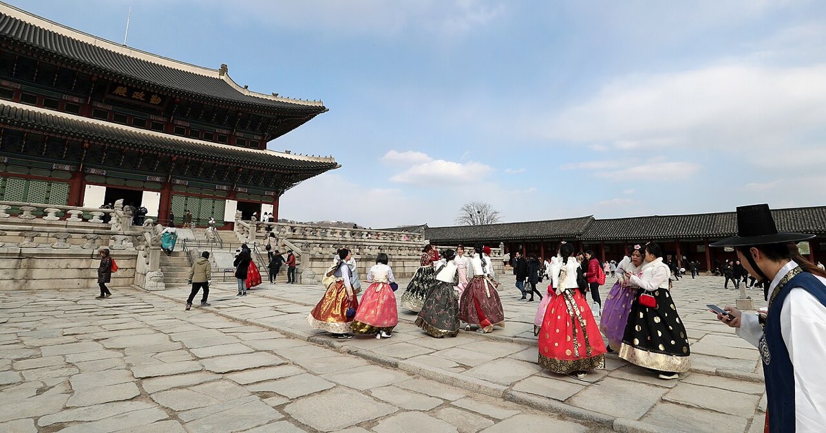 Visitors dressed in hanbok cross the stone-paved courtyard beside Geunjeongjeon, the throne hall of Gyeongbokgung.