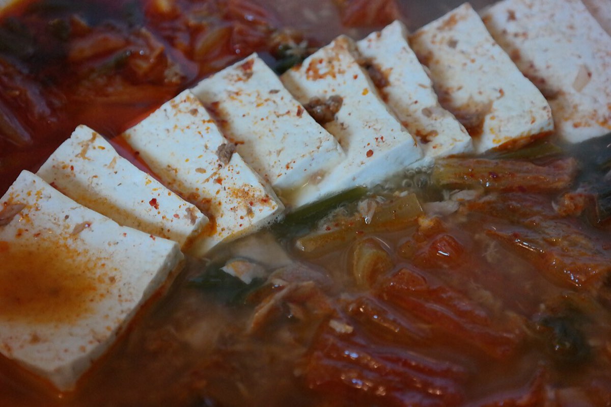Kimchi-jjigae with slices of tofu, its broth turned red by chili flakes and kimchi.