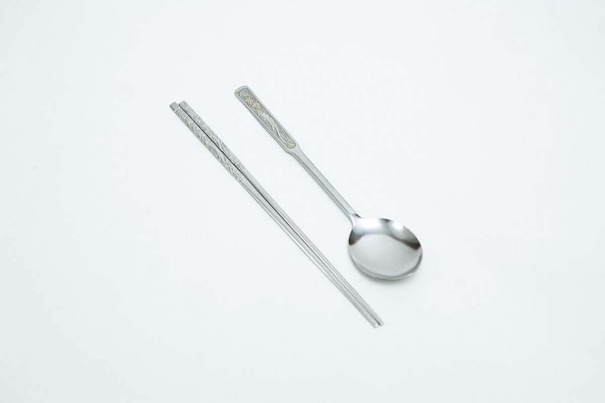A Korean sujeo set: a long-handled metal spoon lying beside a pair of flat metal chopsticks.