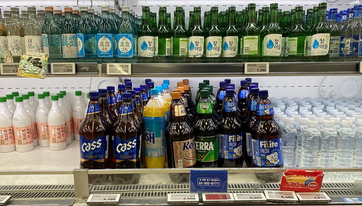 Green bottles of soju above bottles of makgeolli and beer on a store shelf in South Korea.