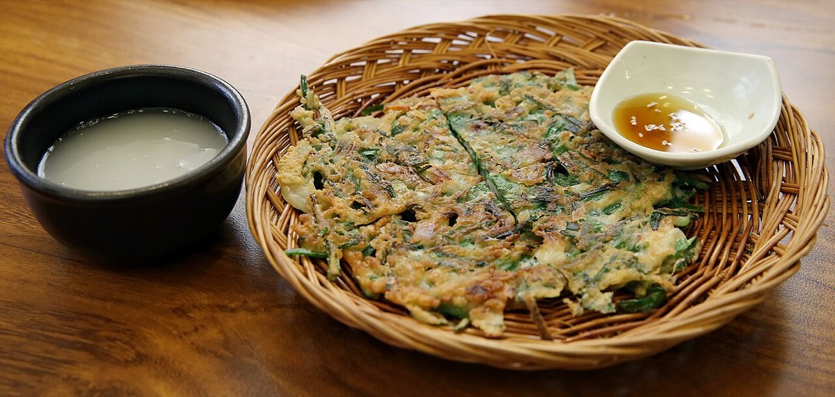 Buchimgae, a savory Korean pancake, served with bowls of makgeolli and a soy dipping sauce.