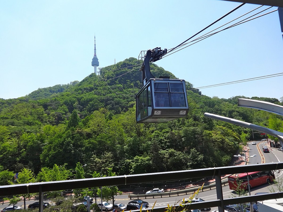 A Namsan cable car cabin climbs the wooded slope toward N Seoul Tower at the summit.