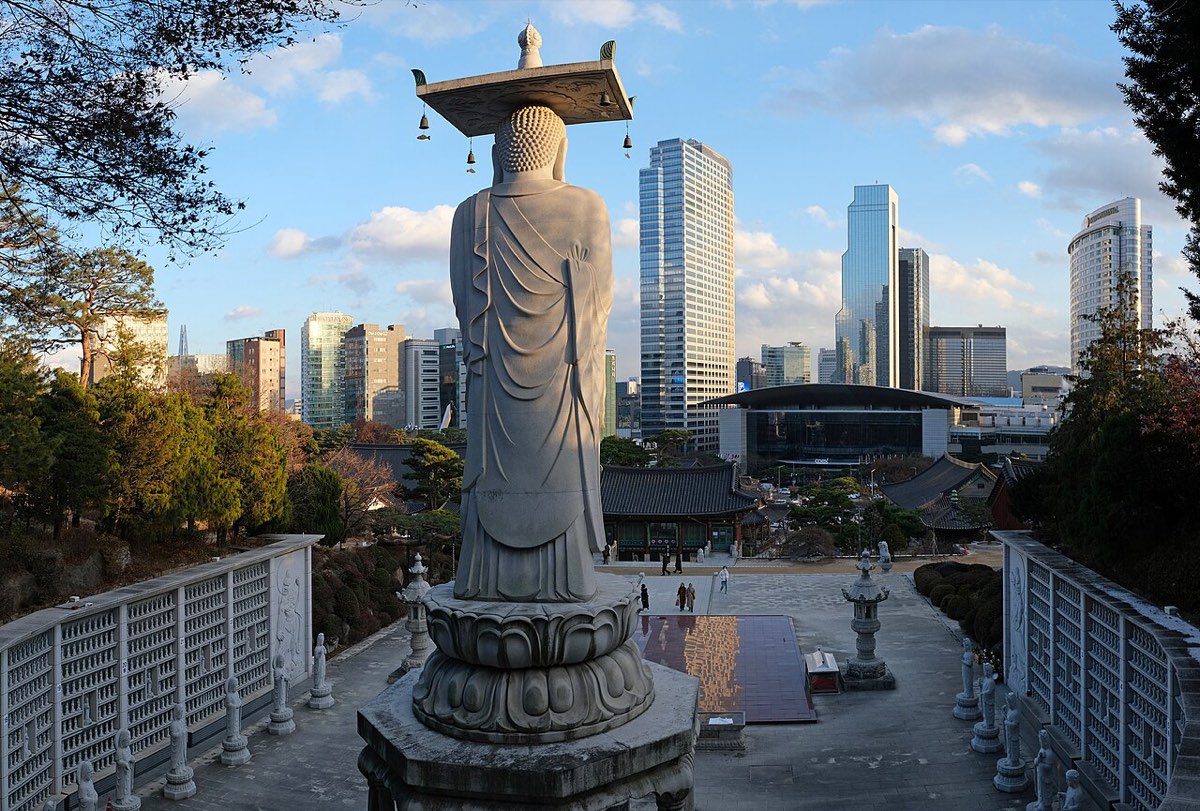 Bongeunsa's giant standing Maitreya statue overlooks the temple grounds, with Gangnam's office towers and COEX beyond.