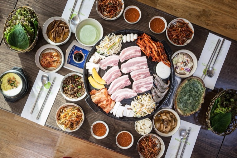 Raw pork belly on a platter surrounded by side dishes, ready for a Korean barbecue grill