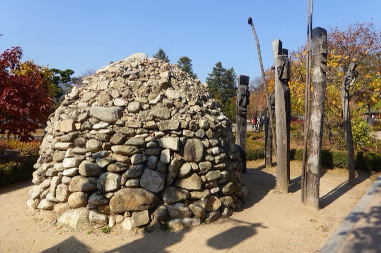 A stone cairn and carved wooden village guardian posts outside the National Folk Museum of Korea