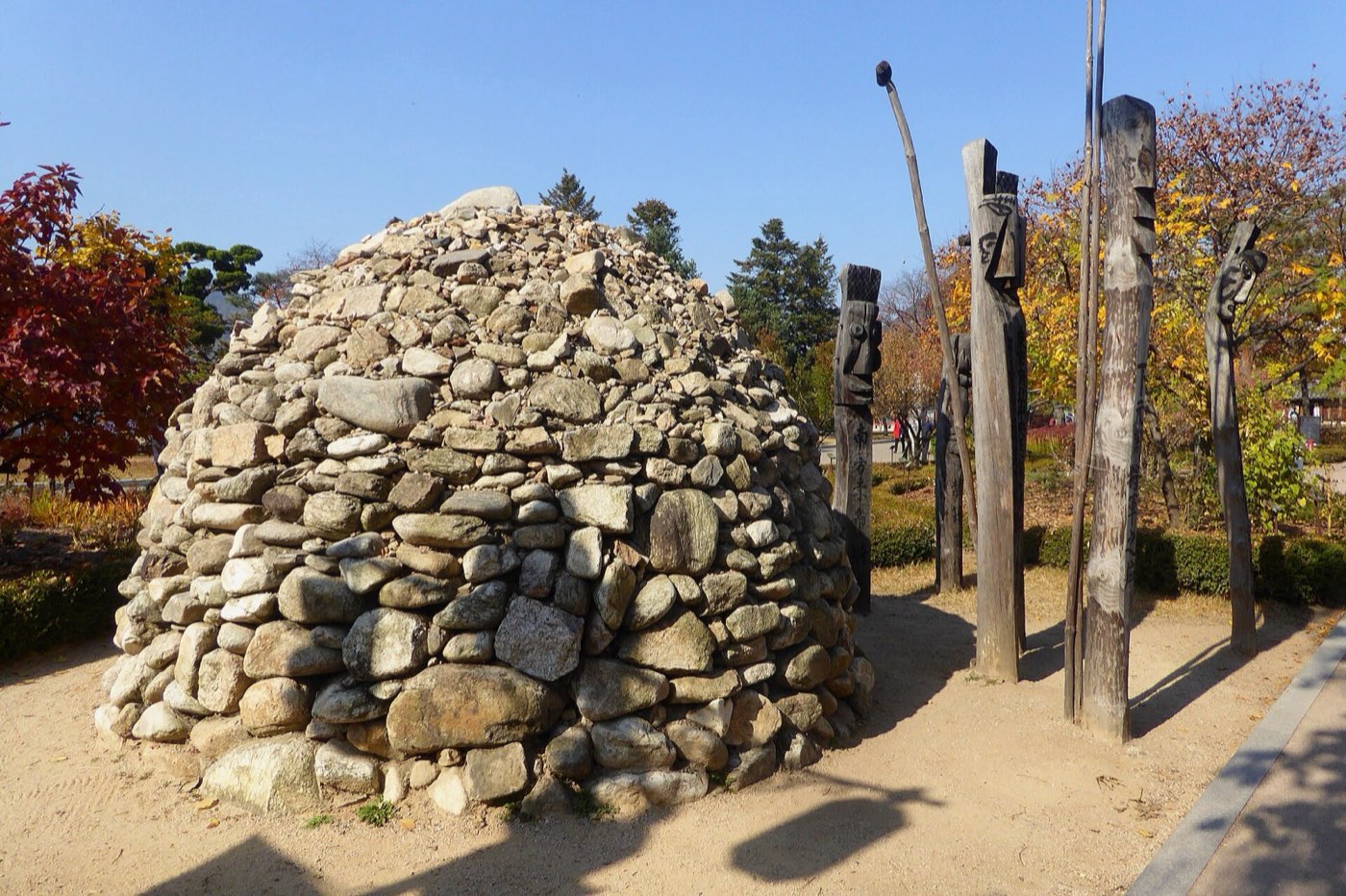 A stone cairn and carved wooden village guardian posts outside the National Folk Museum of Korea