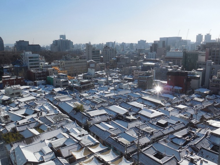 Snow on the tile roofs of Ikseon-dong's hanok lanes, with central Seoul beyond