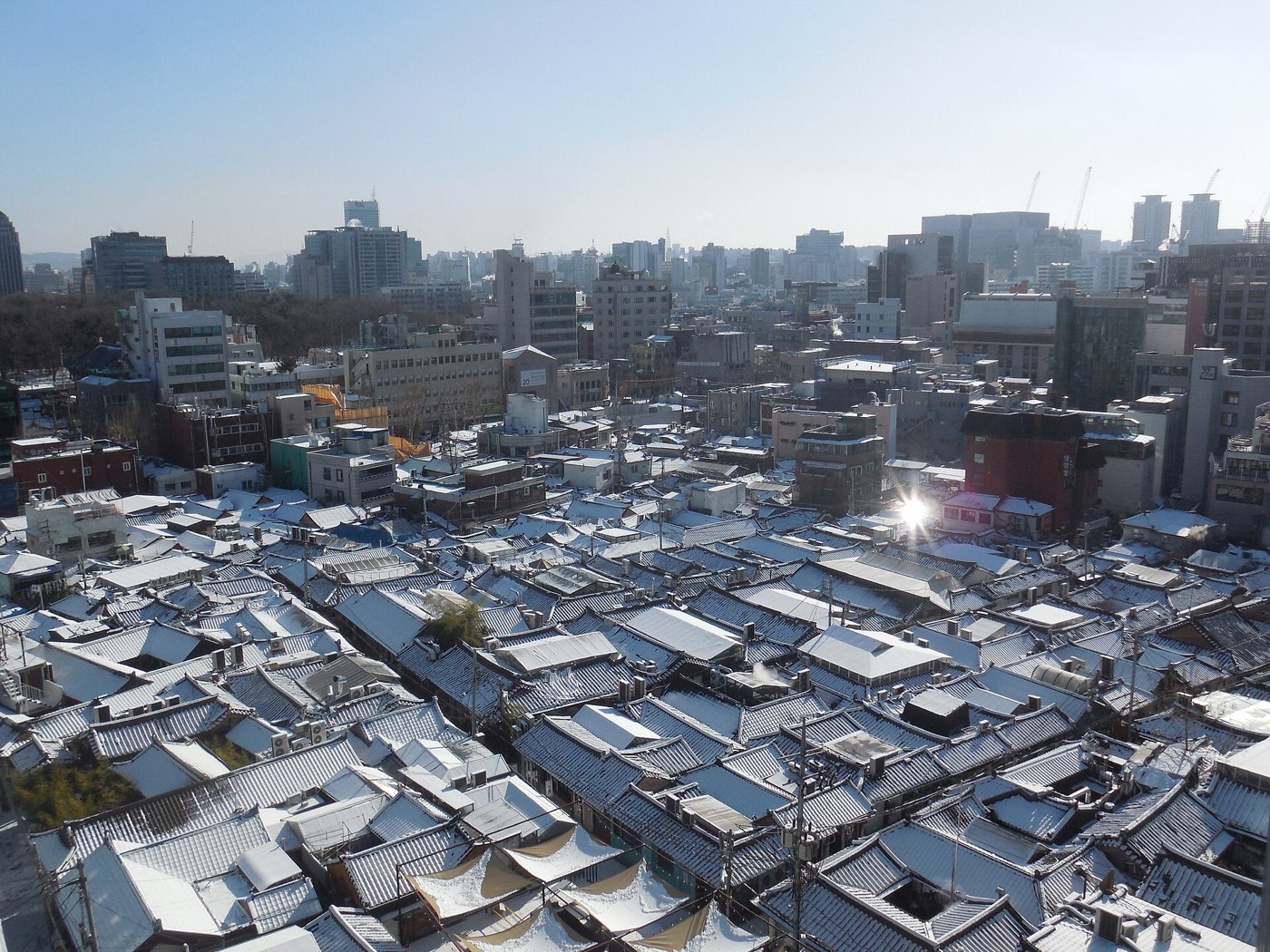 Snow on the tile roofs of Ikseon-dong's hanok lanes, with central Seoul beyond